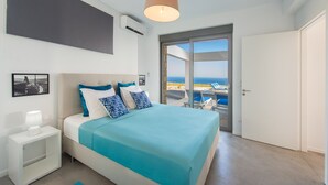 A bedroom with a bed, a nightstand, a lamp, a picture on the wall, and a view of the sea through a glass door. - Villa in Rhodes with Infinity Pool (Kalythies)