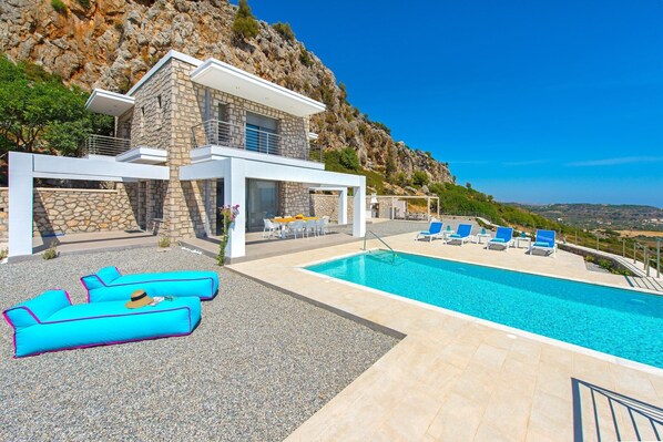 En modern villa med en swimmingpool, utomhusmöbler och utsikt över det omgivande landskapet.