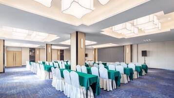 Un salón de conferencias con filas de mesas y sillas, suelo alfombrado y un diseño moderno en el techo.
