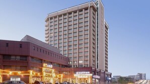 Ein mehrgeschossiges Hotel mit modernem Design, das einen markanten Eingangsbereich mit beleuchteter Beschilderung und einen Parkplatz davor aufweist.