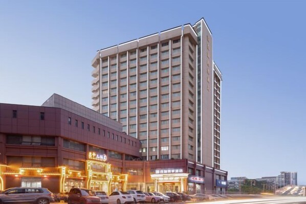 Un hotel de varios pisos con diseño moderno, que cuenta con una entrada destacada con señalización iluminada y un área de estacionamiento al frente.