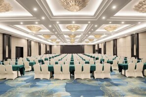 Une salle de conférence avec des rangées de tables et de chaises, une scène et un tapis à motifs.