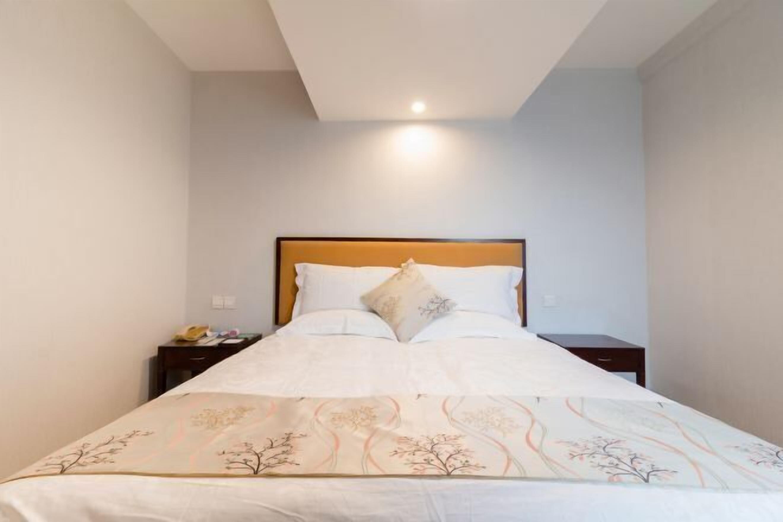 A neatly made bed with a floral bedspread, a wooden headboard, and two bedside tables with lamps.