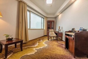 A hotel room with a large window, a desk with a chair, a small table with a plant, and a carpet with a wavy pattern. - Braim Seasons Hotel (Nanchang)