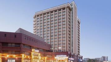 A multi-story hotel with a prominent corner building and a parking lot with several cars.