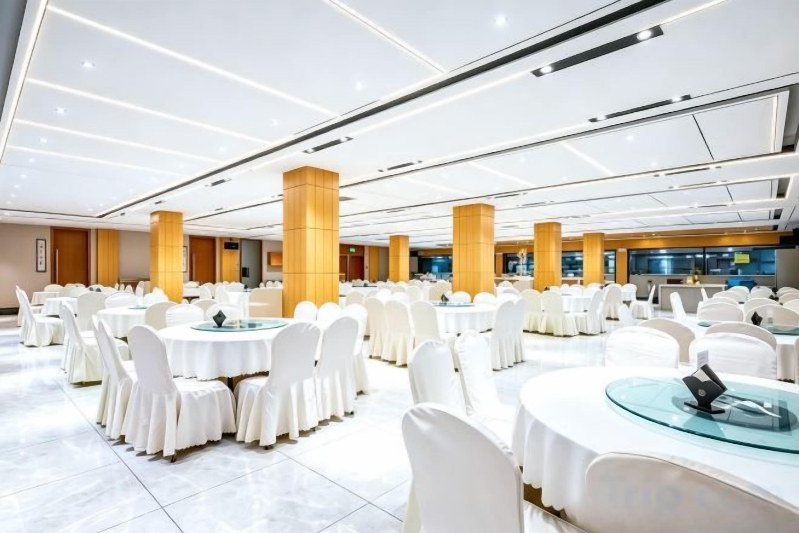 A banquet hall with round tables and white chairs, large pillars, and a modern ceiling design.