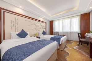 Une chambre d’hôtel avec deux lits, un bureau, une chaise, une grande fenêtre avec des rideaux et un mur orné de calligraphies.