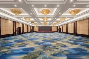 Un amplio salón de conferencias con alfombra estampada, iluminación empotrada y un escenario al frente.