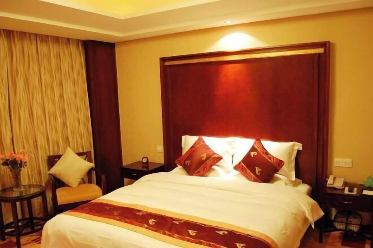 Habitación de hotel con una cama grande, cabecera de madera, una mesita con un florero y una silla.