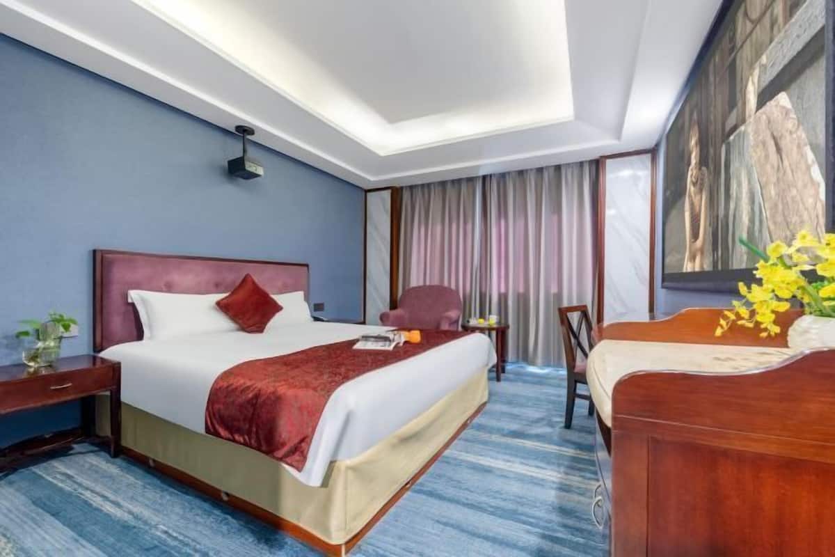 Un cuarto de hotel con una cama grande, un escritorio, una silla, una ventana con cortinas y un cuadro en la pared.