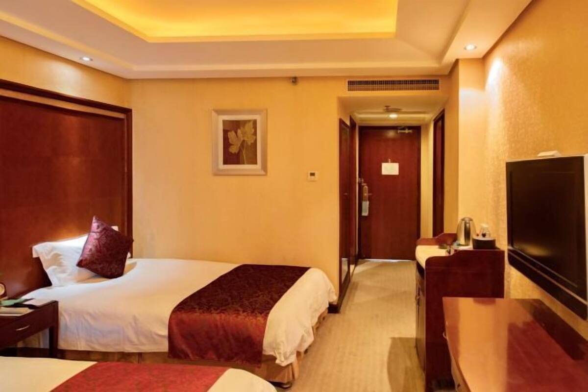 Una habitación de hotel con dos camas, televisión, escritorio y espejo.