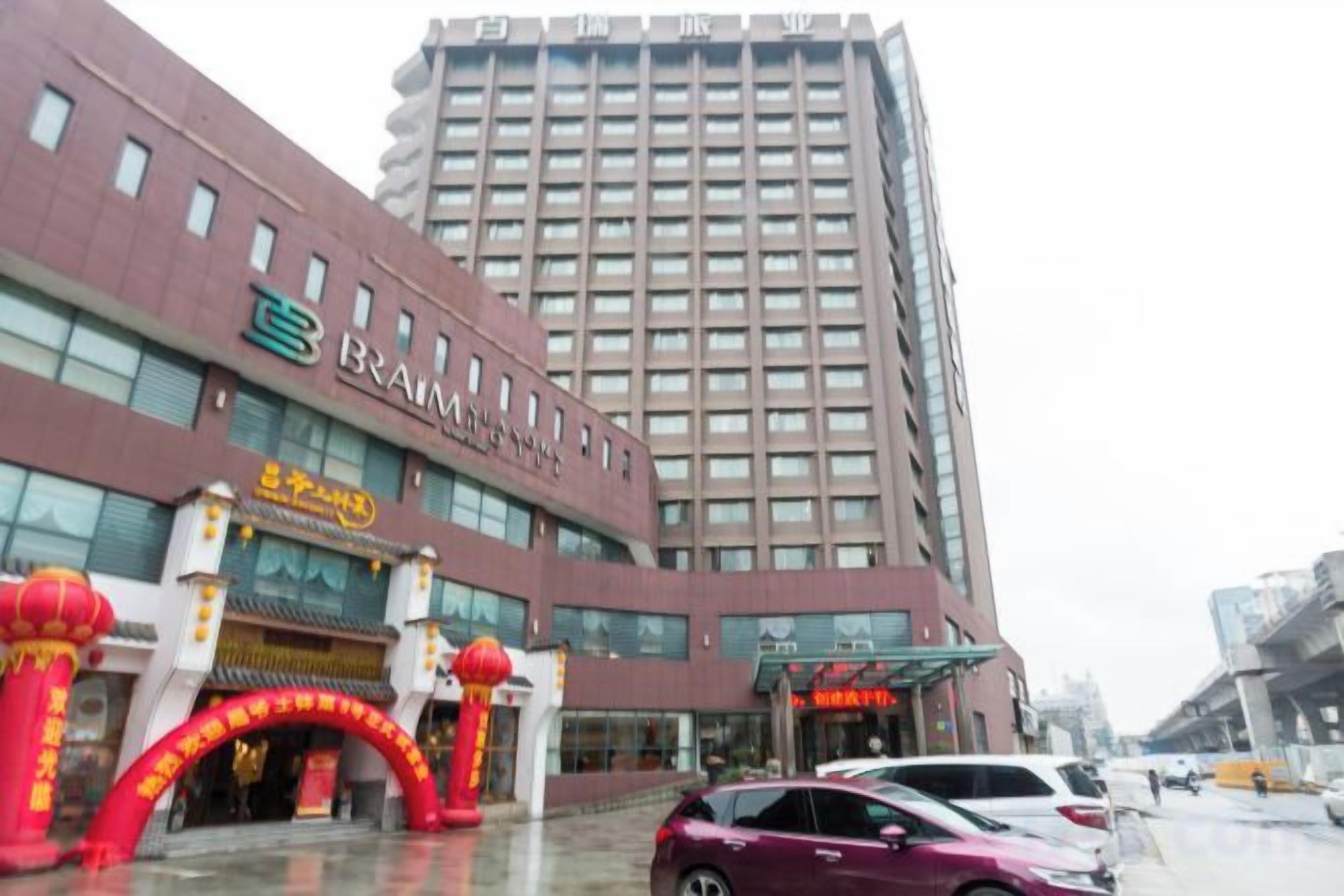 A multi-story hotel building with a prominent sign, a large entrance with red decorations, and a parking area with cars.