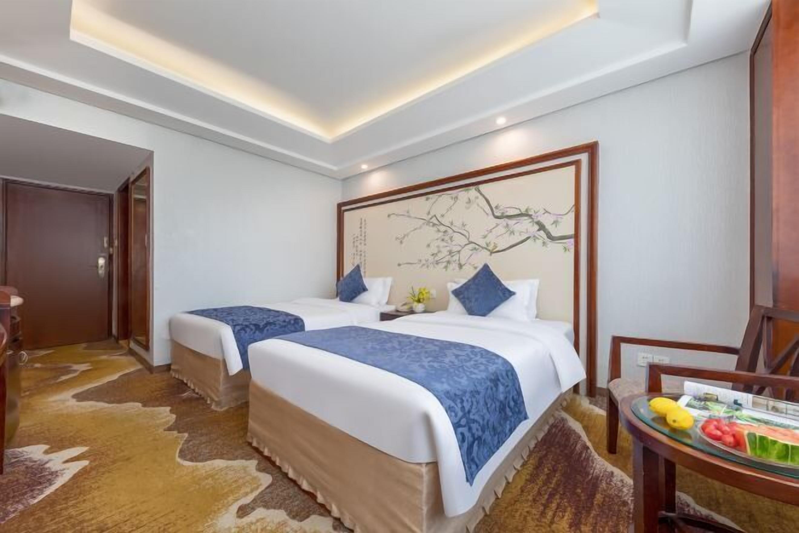 Habitación de hotel con dos camas, cabecera de madera con obra de arte, una mesita con fruta y una alfombra de cuero de vaca.