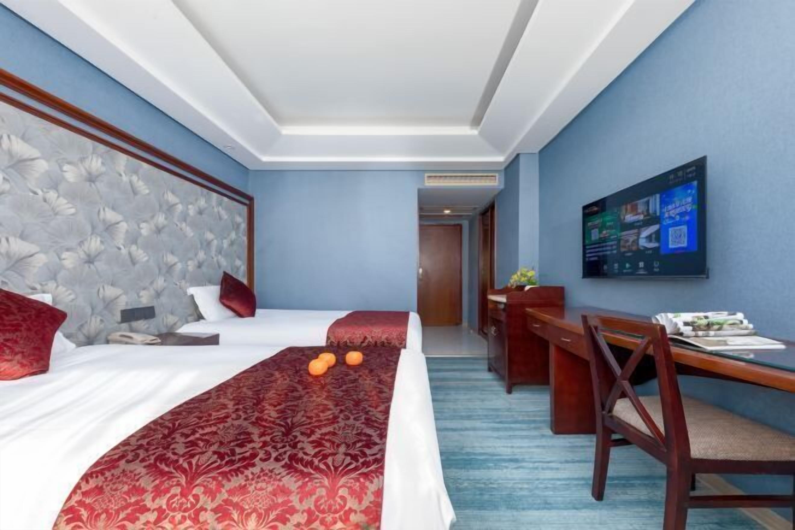 Ein Hotelzimmer mit einem großen Bett, einem Schreibtisch und einem an der Wand befestigten Fernseher.