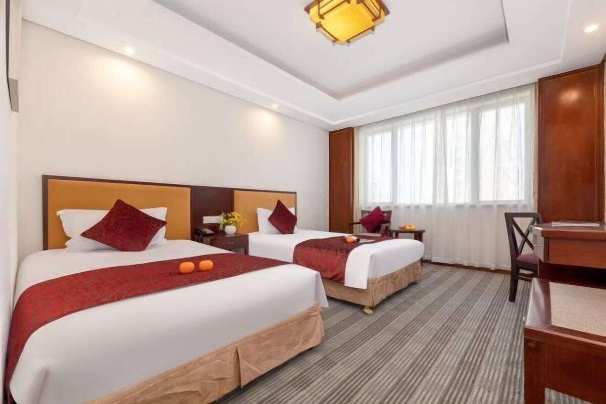 Habitación de hotel con dos camas, un escritorio, una silla, una lámpara y una ventana con cortinas.
