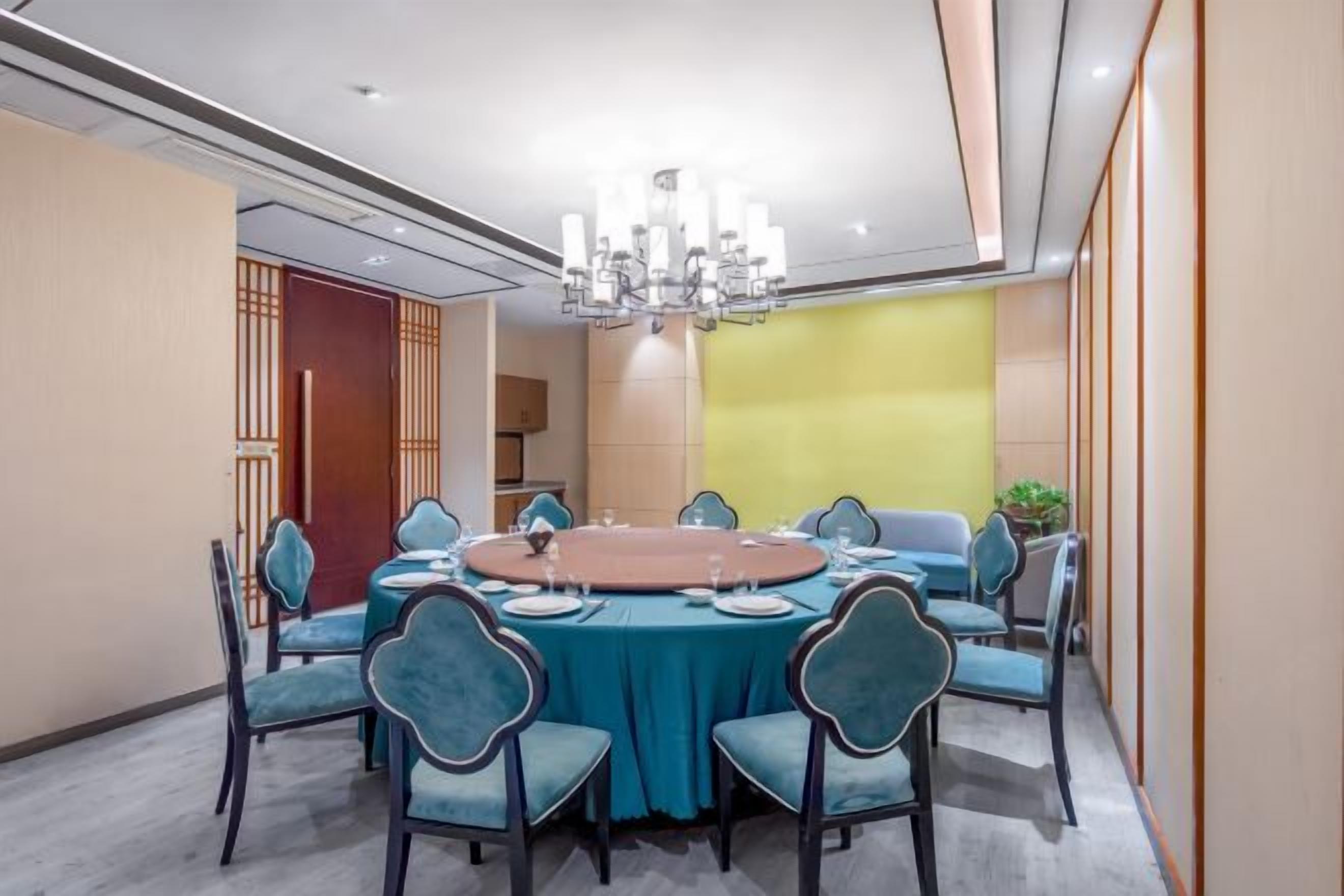 A conference room with a round table, teal chairs, and a chandelier.