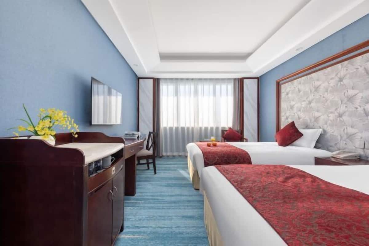 Habitación de hotel con dos camas, un escritorio con silla, un espejo grande y una ventana con cortinas.