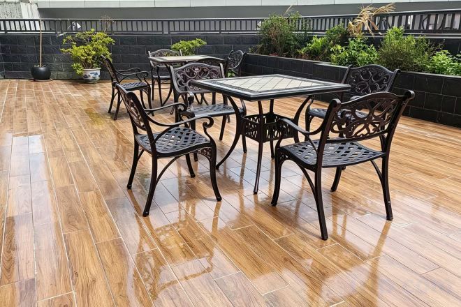 A patio with a table and chairs, surrounded by potted plants and a black wall.