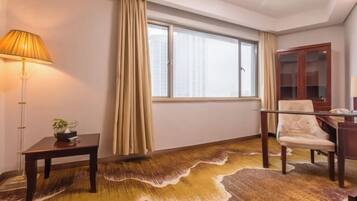 Una habitación de hotel con un ventanal grande, un escritorio de madera, una silla, una lámpara y una alfombra.