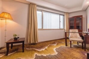 Hotellihuone, jossa on suuri ikkuna, puinen työpöytä, tuoli, lamppu ja matto.