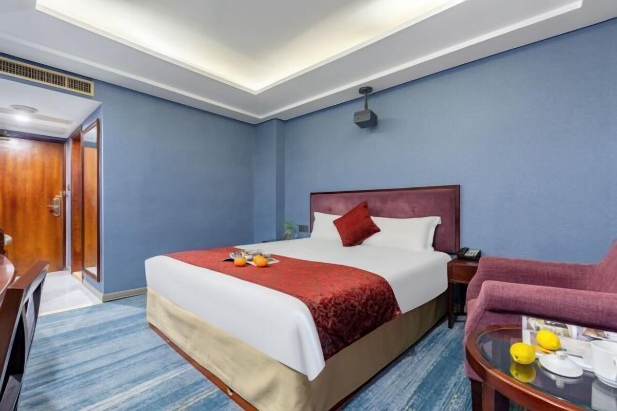 Hotellihuone, jossa on sänky, työpöytä, tuoli ja pieni lasitasoinen sivupöytä.