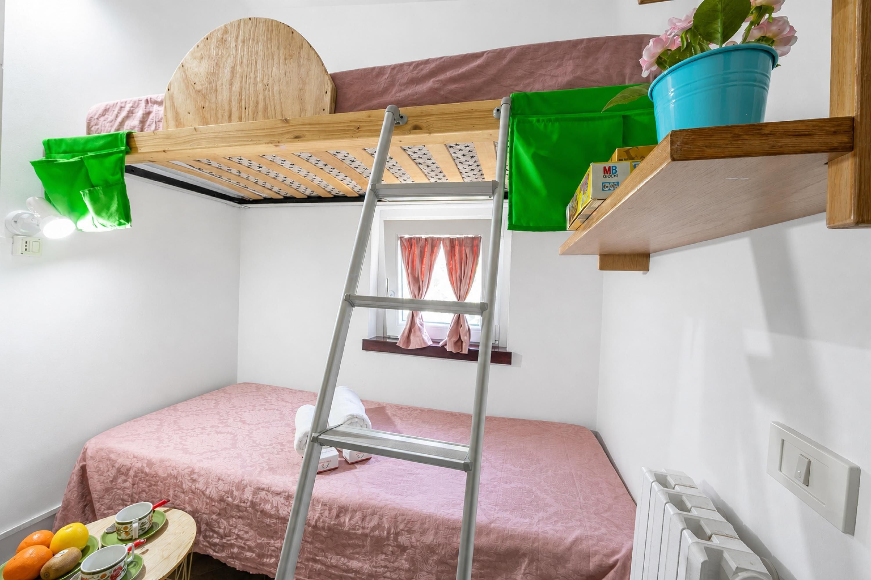 A bunk bed with a ladder, a small table with fruit, a potted plant, and a window with curtains.