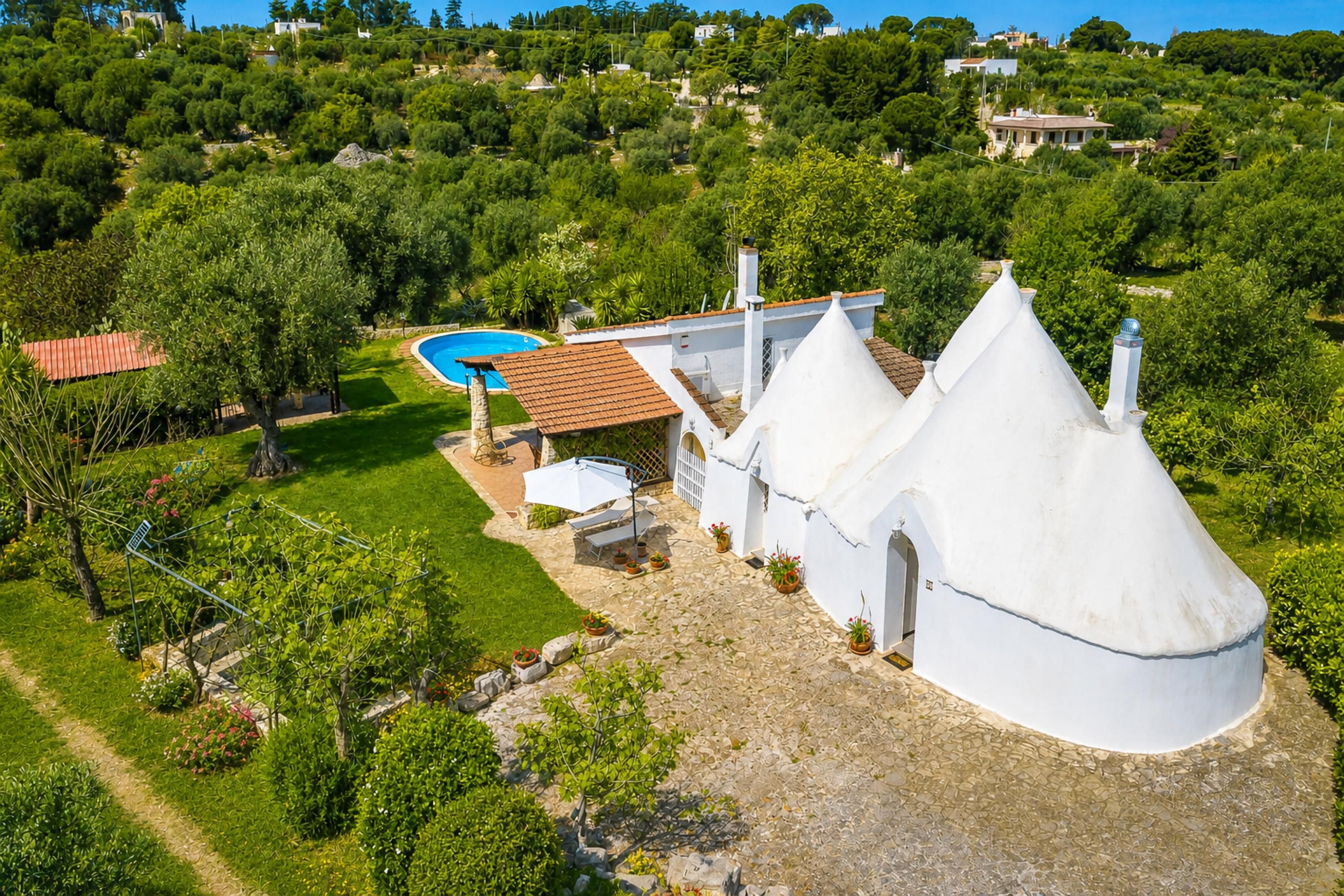 Une villa blanche dotée d’une piscine, entourée d’une végétation luxuriante et d’un paysage vallonné.