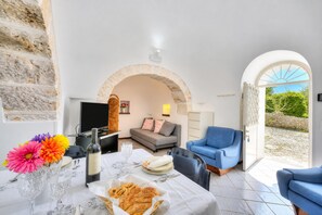 A dining area with a table set for two, a sofa, and a TV in the background. - La Casa Sulla Roccia Trulli Pool (Monopoli)