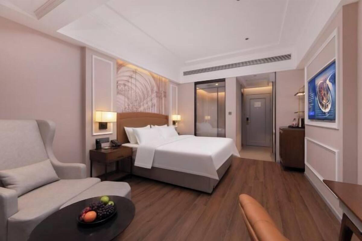 A hotel room with a bed, a sofa, a desk, a fruit bowl, and a painting on the wall.