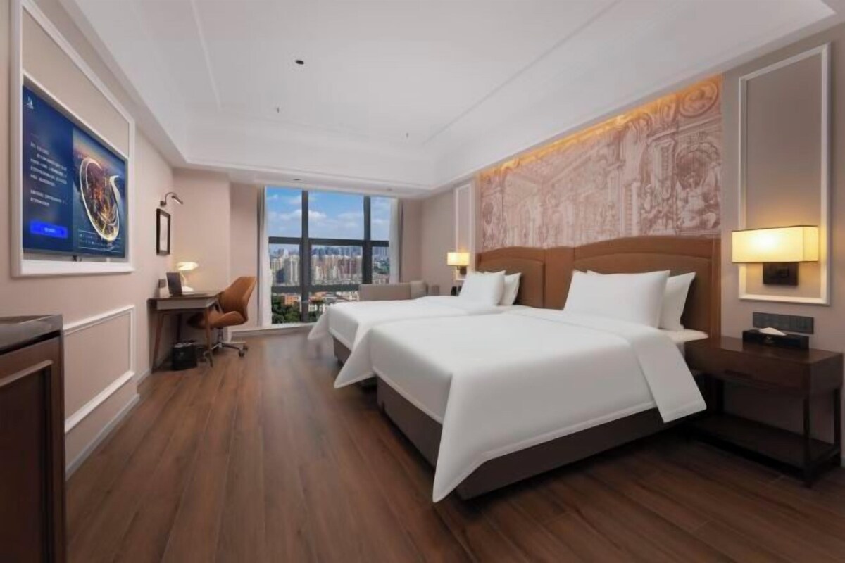 Habitación de hotel con una cama grande, un escritorio, una silla y vistas a la ciudad.