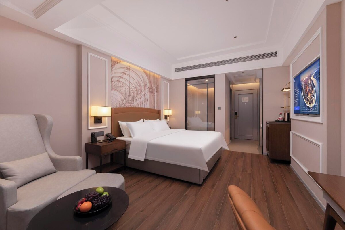 Une chambre d’hôtel avec un lit, une chaise, un bureau et une petite table sur laquelle se trouvent des fruits.