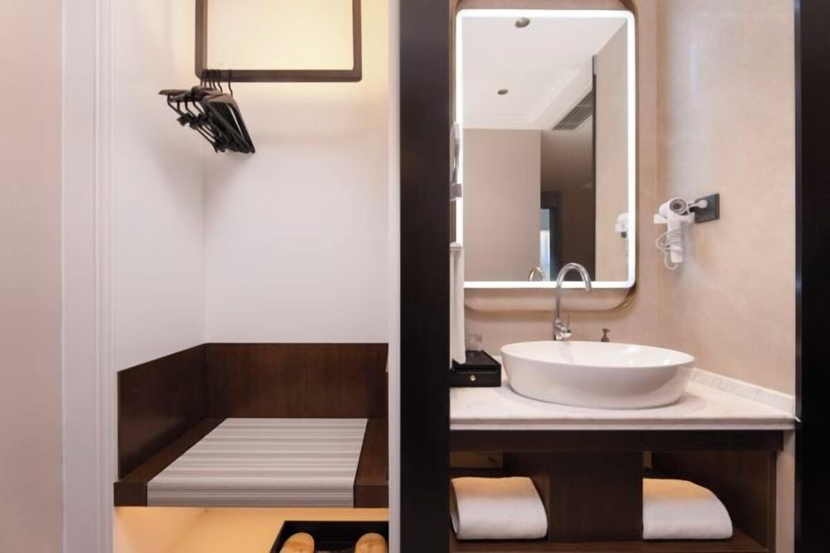 Un baño moderno con un espejo grande, un lavabo blanco y un banco de madera.