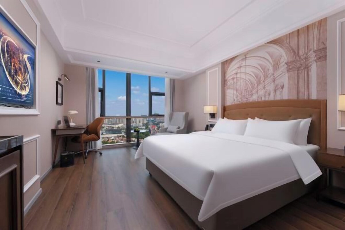 Habitación de hotel con una cama grande, un escritorio, una silla y vistas a la ciudad.