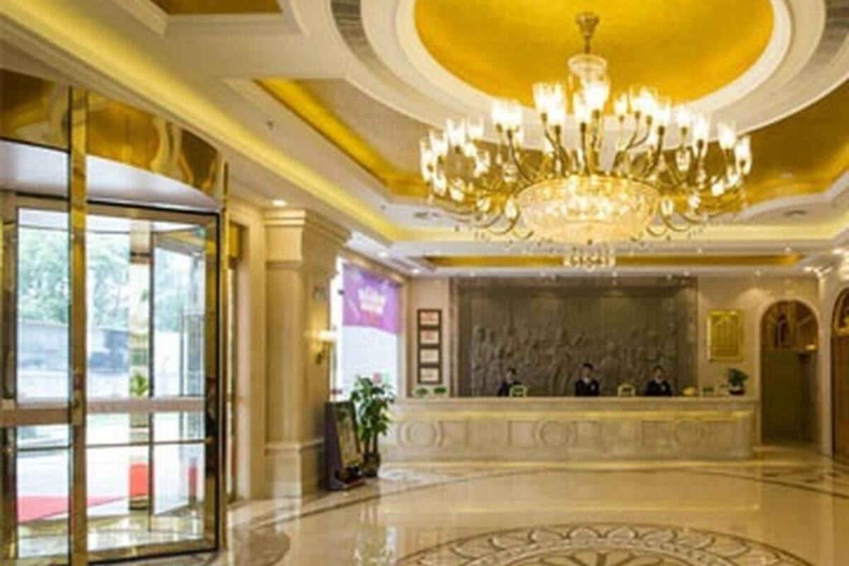 A hotel lobby with a grand chandelier, a reception desk, and a marble floor.