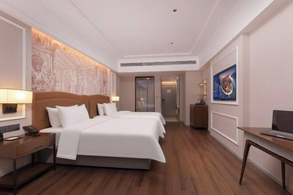 A hotel room with a large bed, a desk, a chair, a telephone, and a wall-mounted artwork.