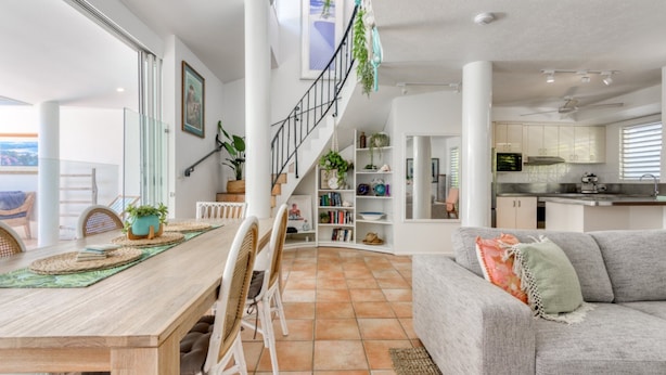 A modern living space with a wooden dining table, white chairs, a grey sofa, and a staircase leading to an upper level. - Donovan's Reef | Port Douglas (Port Douglas)
