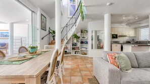 A modern living space with a wooden dining table, white chairs, a grey sofa, and a staircase leading to an upper level.