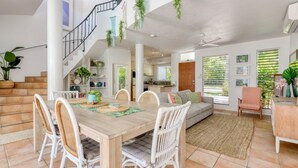 A spacious living area with a wooden dining table, white wicker chairs, a grey sofa, and a staircase with hanging plants. - Donovan's Reef | Port Douglas (Port Douglas)