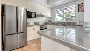 A modern kitchen with stainless steel appliances, white cabinets, and a large island. - Donovan's Reef | Port Douglas (Port Douglas)