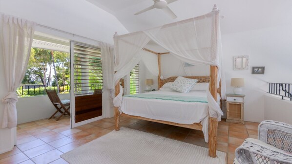 A bedroom with a four-poster bed, a balcony with a chair, and a ceiling fan.