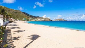 A beach with clear blue water, a sandy shore, and a mountain in the background.