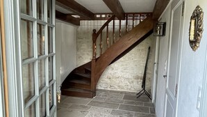 Un pasillo con suelo de piedra, escalera de madera y puerta con paneles de vidrio.