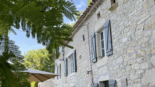 Un edificio de piedra con patio, mesas al aire libre y una pérgola.