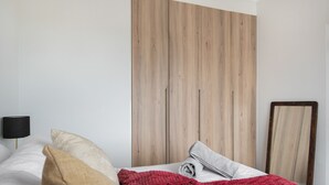 Une chambre à coucher avec une tête de lit en bois, un lit recouvert de draps blancs, une couverture rouge et un miroir accroché au mur.