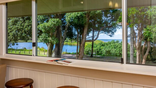 Quarto com uma janela ampla que dá para um lago, árvores e um gramado.