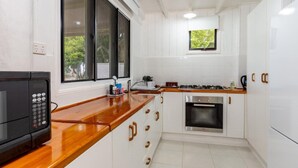 Uma cozinha com armários brancos, bancada de madeira, micro-ondas, fogão e janela com vista para o verde.