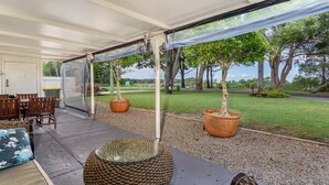 Uma área de varanda coberta com mesa e cadeiras, plantas em vasos e vista para a paisagem ao redor.