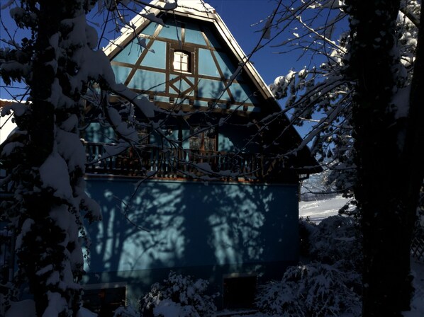 Een klassiek chalet met een steil dak, houten balkon en besneeuwde omgeving.