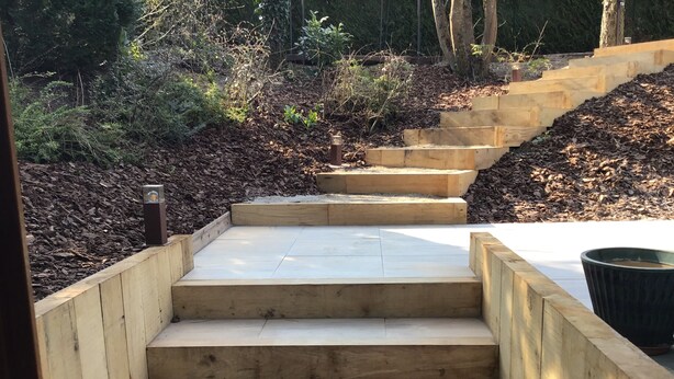 Un ensemble de marches en bois menant à une plateforme en béton, entourée de paillis et de plantes.