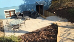 Un espace patio aménagé avec du mobilier d’extérieur, une table en verre et un petit jardin.